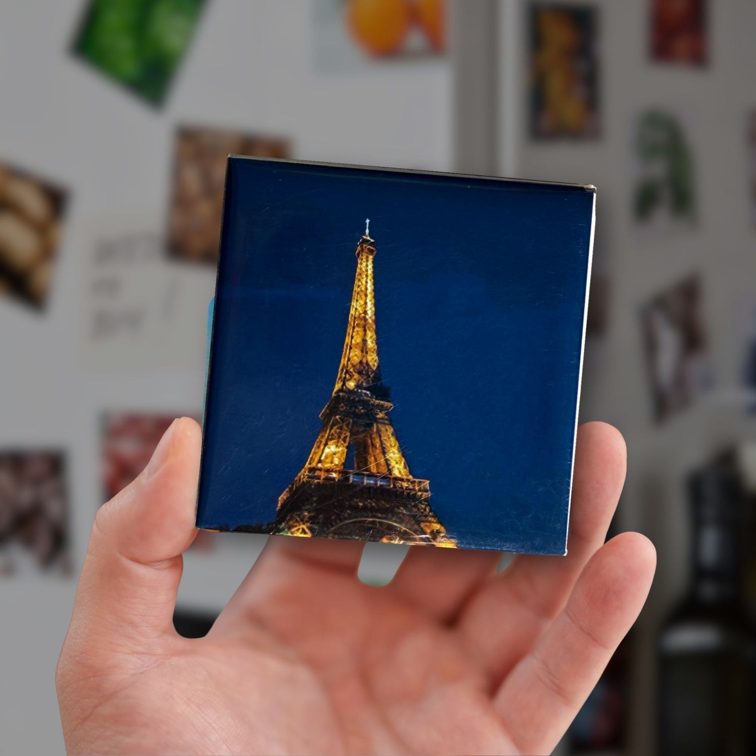 Hand holding a small square magnet with an image of the Eiffel Tower.